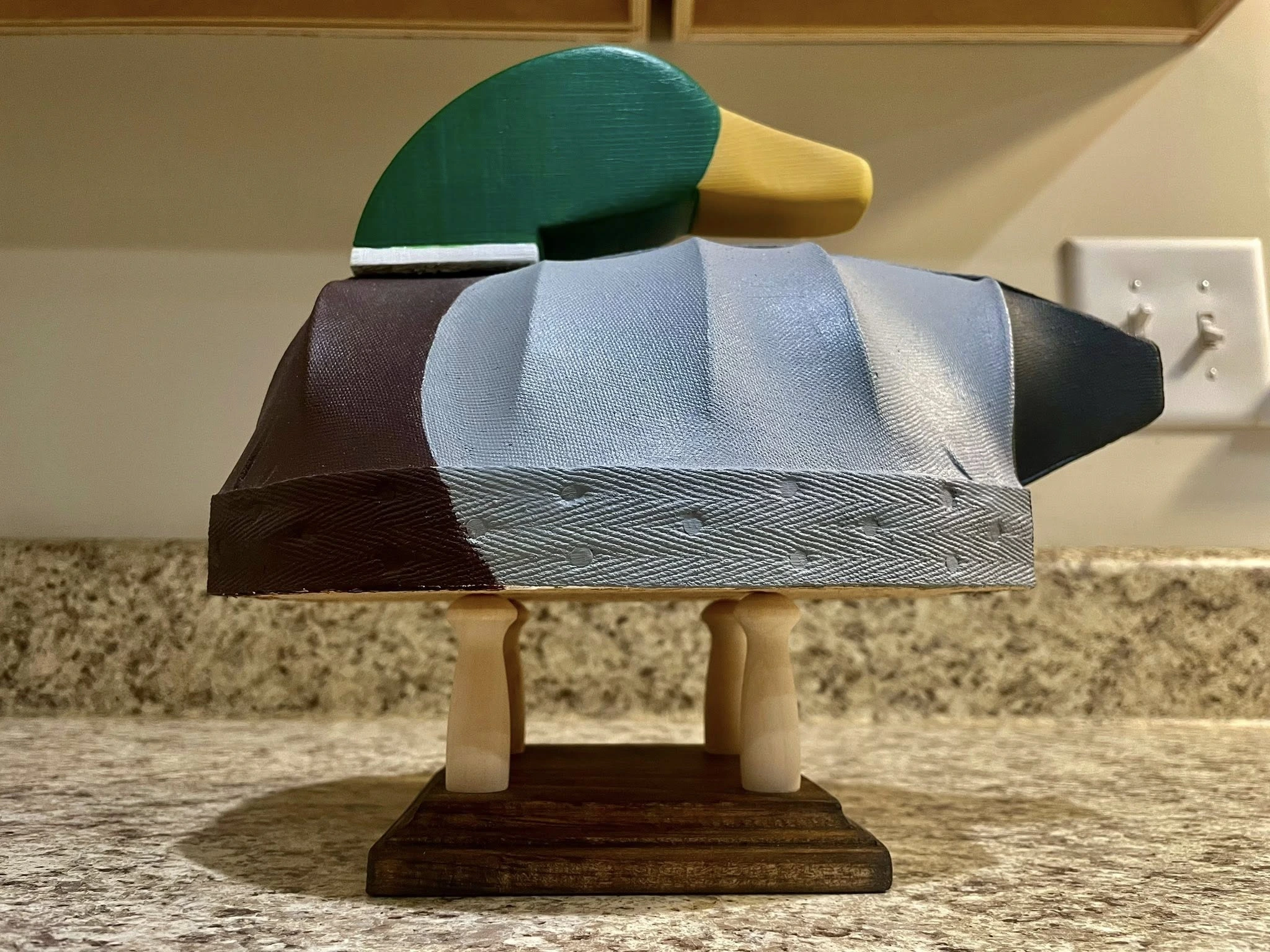 Hand carved canvas mallard decoy displayed on a wooden stand.